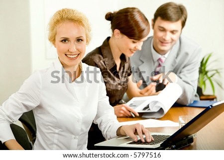Young attractive office worker is sitting at the table on the background of her colleagues