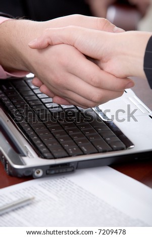 Business people shaking hands above the keyboard of laptop