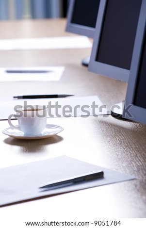 Image of cup, papers, pens and monitors placed on a table