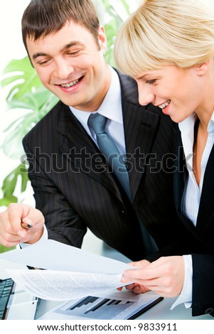 Vertical image of two smiling business colleagues discussing business documents in the office