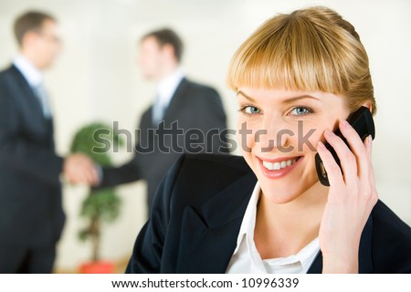 View of attractive smiling businesswoman speaking on the mobile looking at camera