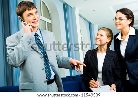 Portrait of busy man talking on the cell while two young pretty women standing near by and looking at him