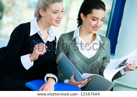 Photo of two businesswomen sitting in the office and doing some paperwork
