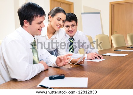 Photo of two men sitting at table and looking at document in secretary’s hand during meeting
