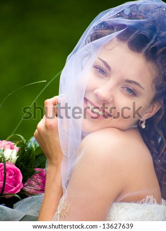 Portrait of gorgeous wife with bouquet looking at camera through veil