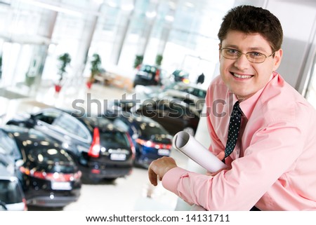 Portrait of happy businessman in the trade centre on the background of different cars