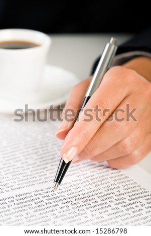 Close-up of femaleâ??s hand holding pen over business document with cup of coffee near by