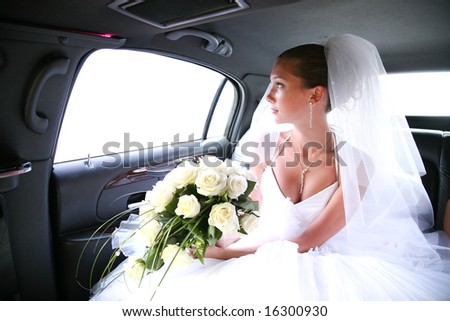 Portrait of beautiful bride with rose bouquet in hands sitting in the car and looking aside