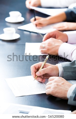 Close-up of line of hands with pens over papers on the table