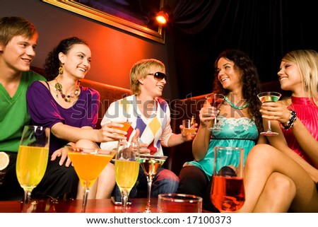 Portrait of friends sitting on the sofa and holding the cocktails in the nightclub