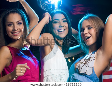 Portrait of three laughing girls dancing at disco in the night club