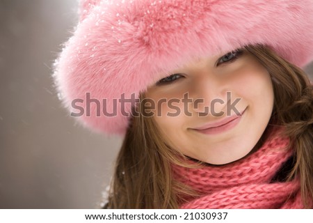 Face of pretty woman wearing pink winter fur cap and looking at camera with smile
