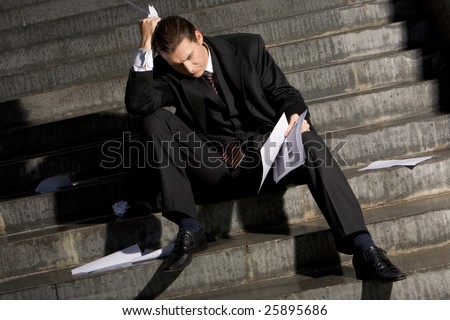 Photo of sad man with papers in hands sitting on stairs with no idea what to do