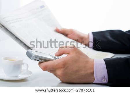 Close-up of male hand pressing keys of smartphone while reading paper
