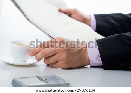 Close-up of male hand on cup of coffee during reading of paper