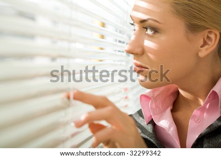 Image of pretty businesswoman looking through venetian blind in office