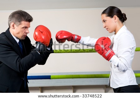 Portrait of aggressive businessman in boxing gloves with serious female opposite him