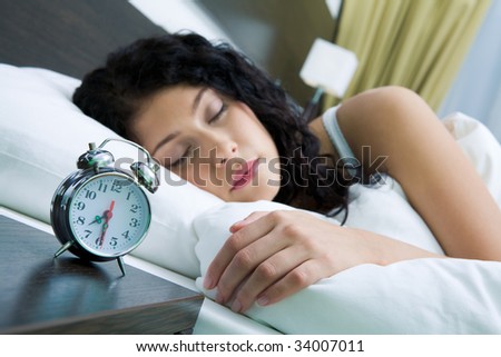 Image of alarm clock on background of sleeping female in the morning