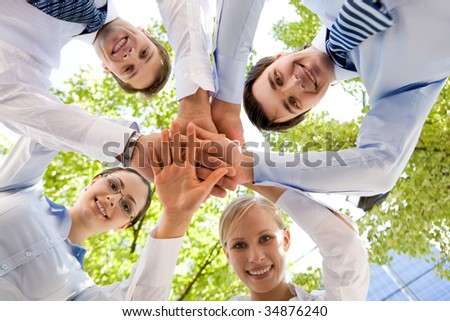 Bottom view of people making pile of hands on background of green foliage
