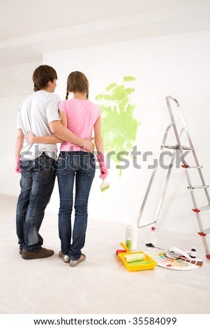 Rear view of embracing couple looking at wall with green paint on