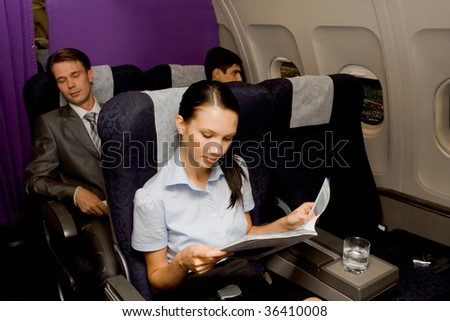 Image of pretty girl reading magazine in airplane with sleeping men behind