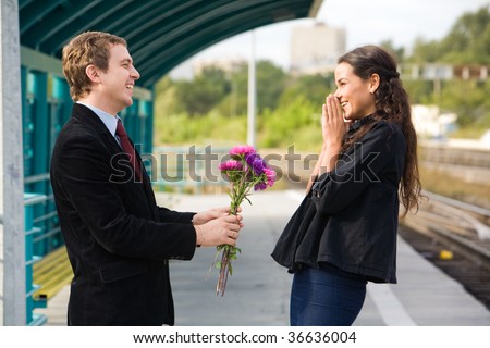 Photo of attractive couple laughing outdoors while guy giving aster bouquet to his sweetheart