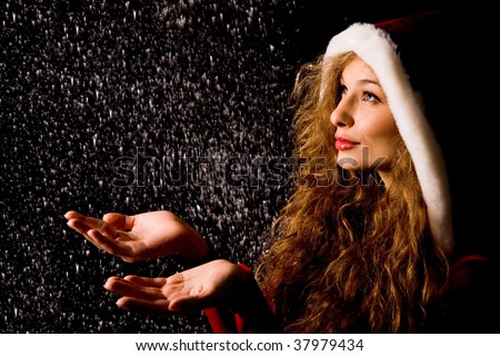 Portrait of pretty girl with open palms catching falling snow over dark background