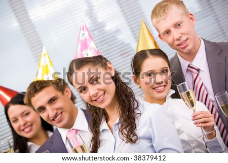 Portrait of joyful friends wearing birthday caps and holding glasses with champagne