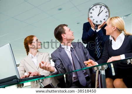 Friendly group of specialists looking at businessman showing clock with lunch time