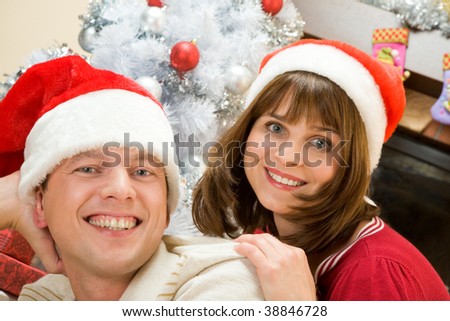 Portrait of happy husband and wife wearing Santa caps and looking at camera