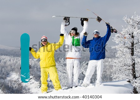 Portrait of three happy young men with snowboards raising their arms
