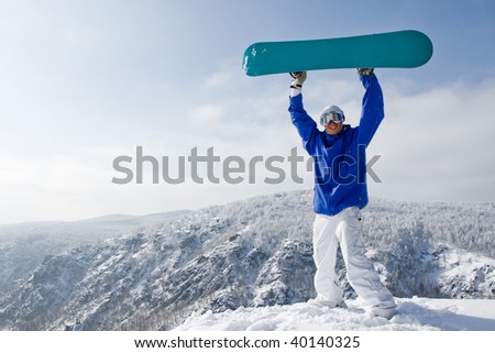 Portrait of joyful sportsman with snowboard standing on top of mount