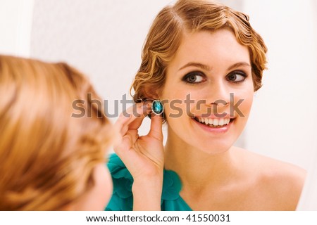 Image of pretty female looking in mirror and putting on earrings
