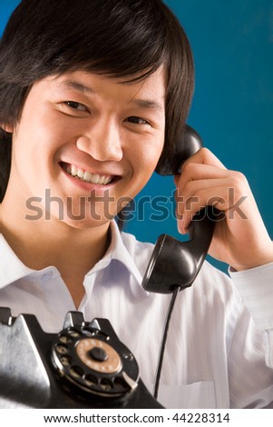Image of happy Asian man holding telephone receiver and smiling