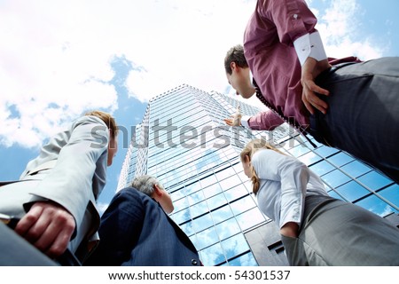 Below view of business partners pointing at modern office building against cloudy sky