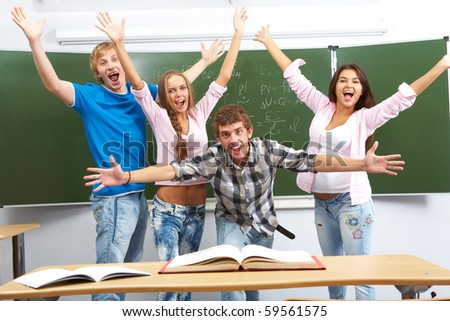 Portrait of four excited teens standing by the blackboard with raised arms