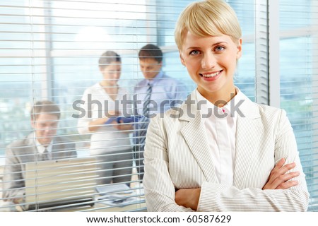 Female leader looking at camera with team of partners working in office behind