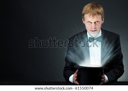 Image of male magician holding hat with magic light and looking at camera