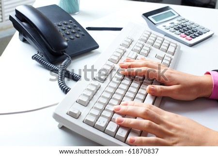 Table with a telephone, calculator, computer keyboard and female hands typing on it