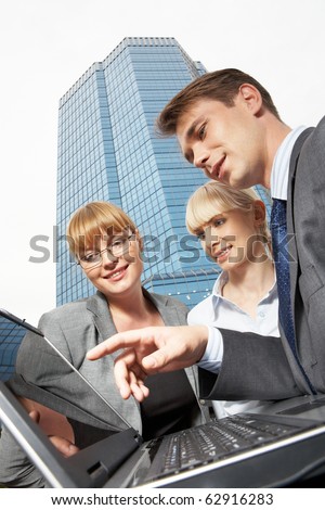Three businesspeople working on computer against an office building