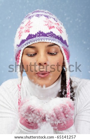 Image of pretty woman in pink gloves and knitted winter cap blowing snow from her palms