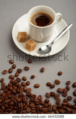 Photo of cup of black coffee with two pieces of sugar and brown beans near by