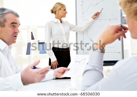 Image of successful businesswoman standing by whiteboard while her colleagues listening to her