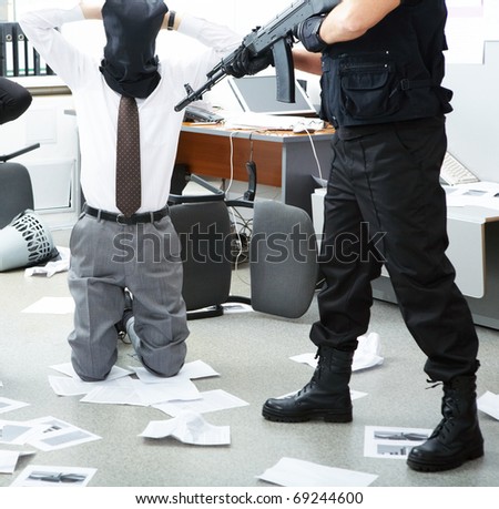 Photo of kneeling businessman wearing black sacks on head with burglar standing near by