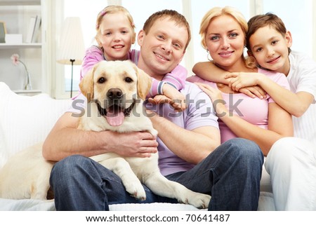 A happy family of four with a dog sitting on sofa, looking at camera and smiling
