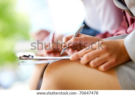 Close-up of hands with pens and legs in line outdoor