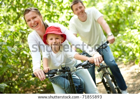Portrait of happy woman with son riding a bicycle in park on background of male