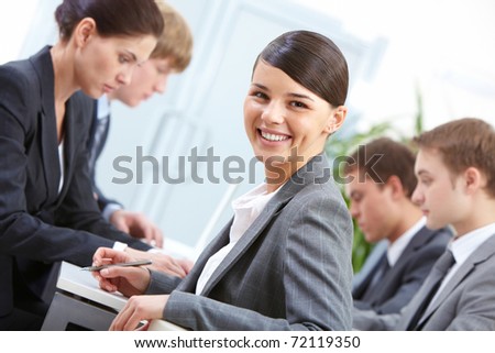 Portrait of beautiful secretary looking at camera on the background of co-workers