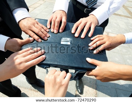 Close-up of people hands holding black leather briefcase simultaneously