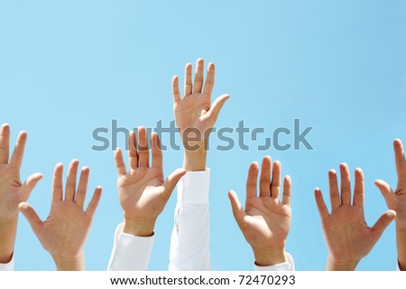 Close-up of several human hands raised against clear blue sky